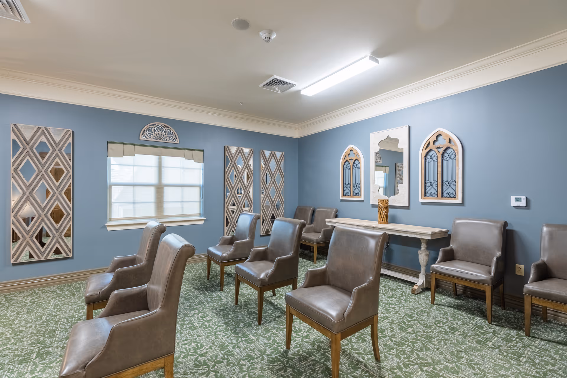 A seating room with multiple leather chairs arranged in rows against blue walls decorated with mirrors and a console table.