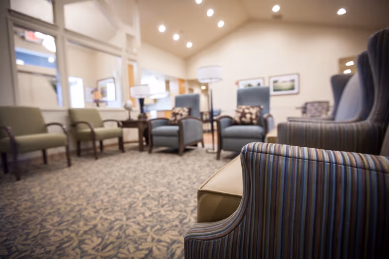Bright seating area in a senior living facility with upholstered armchairs, side tables, and floor lamps.