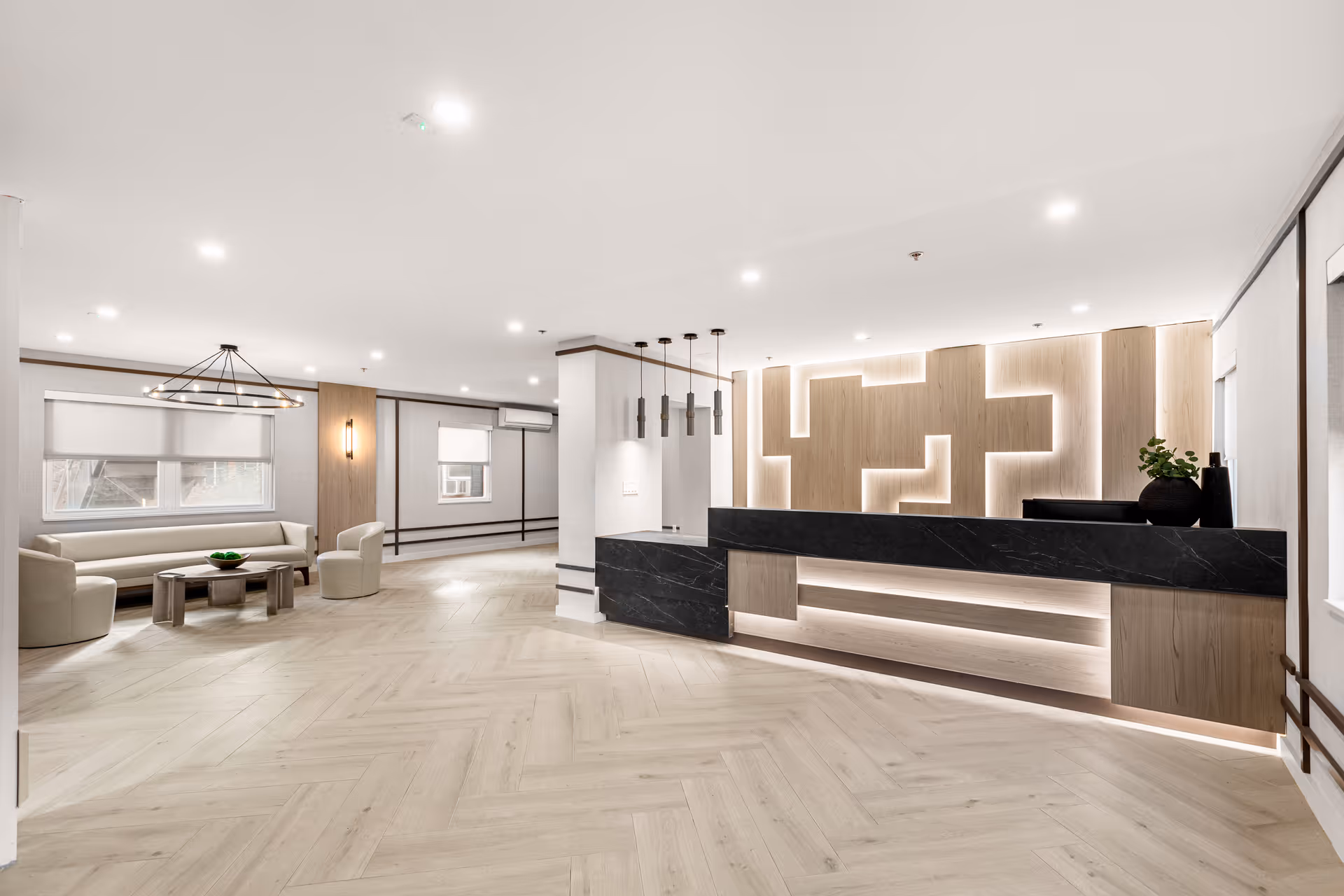 Bright modern reception lobby with a long black marble front desk, illuminated wood feature wall, and a seating area with chairs and a sofa.