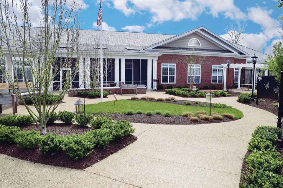 Senior living facility exterior with brick entrance, curved walkway, and manicured landscaping.
