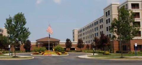 Brookdale Trillium Crossing facility with flag, trees, and a beige multi-story building.