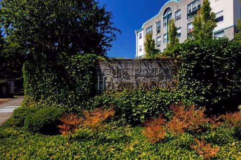 Front view of Hazelwood Community Apartments sign overgrown with ivy beside a multi-story building