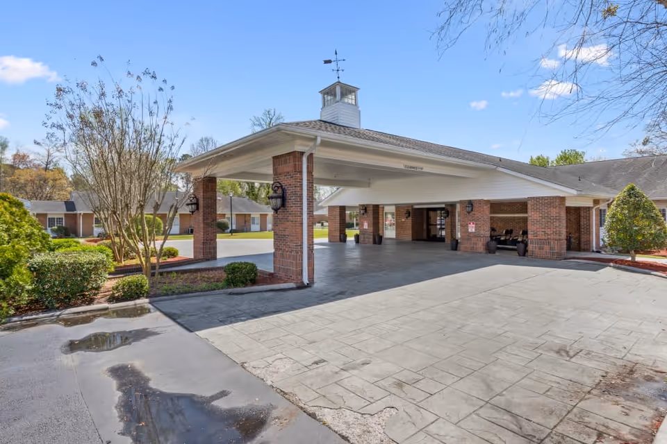 Front entrance porte-cochere of a brick senior living facility with a paved driveway and landscaped grounds.