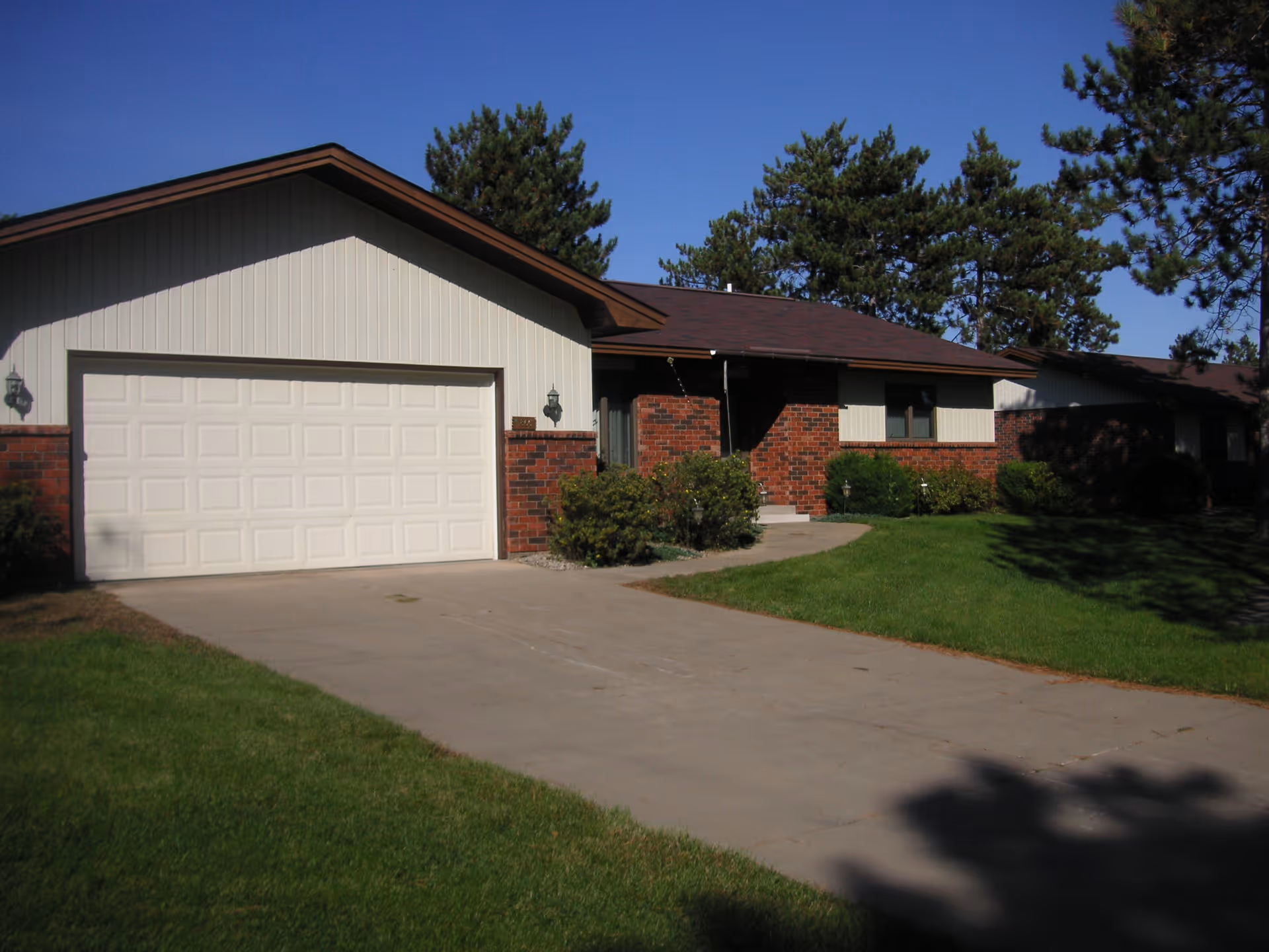 Single-story brick and siding house with an attached two-car garage, driveway and front lawn under a clear blue sky.