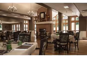 Spacious dining room with multiple set tables, upholstered chairs, chandeliers, and a central fireplace under a high ceiling.