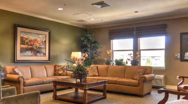 Cozy communal living room with two tan sofas, a wooden coffee table, plants, and framed artwork on the wall.