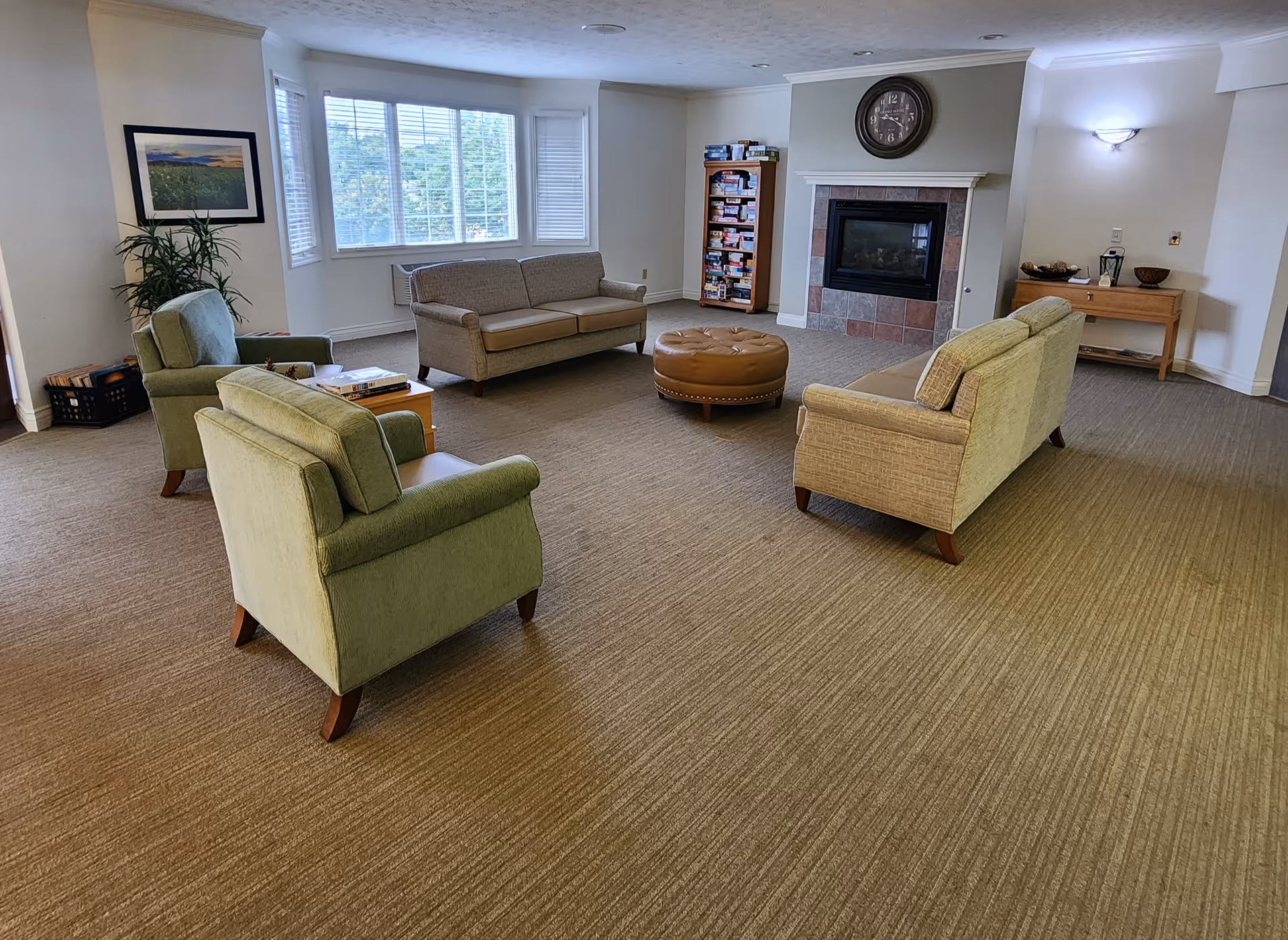 Spacious lounge with sofas and armchairs arranged around a central ottoman in front of a fireplace and a large window.