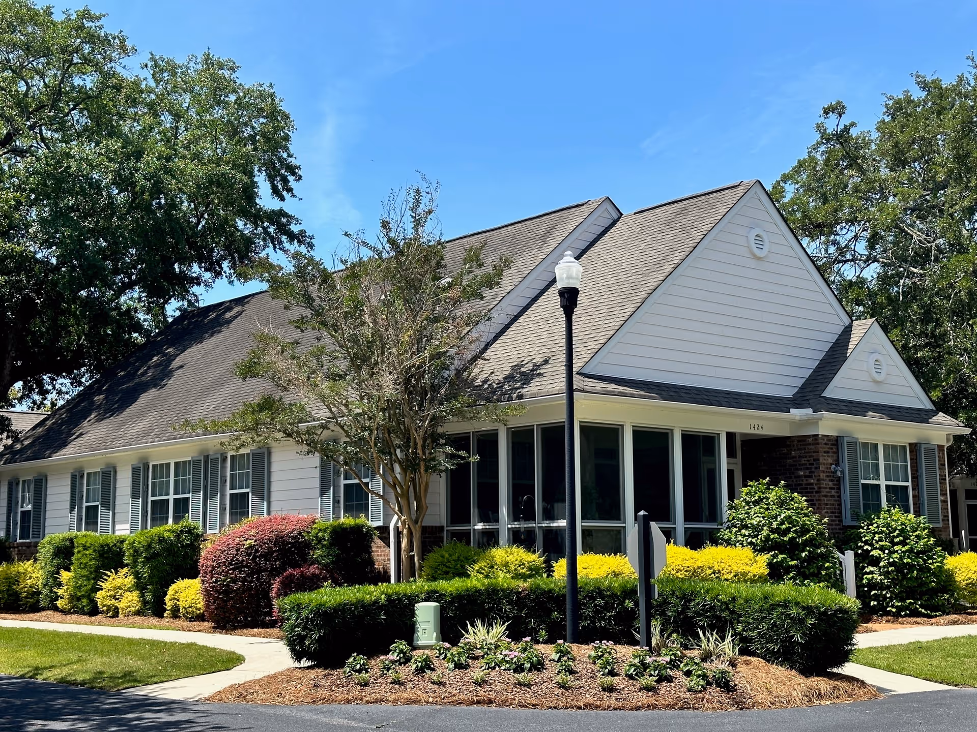 Front exterior of a single-story building with a pitched roof, large windows, landscaped shrubs, and a streetlamp.