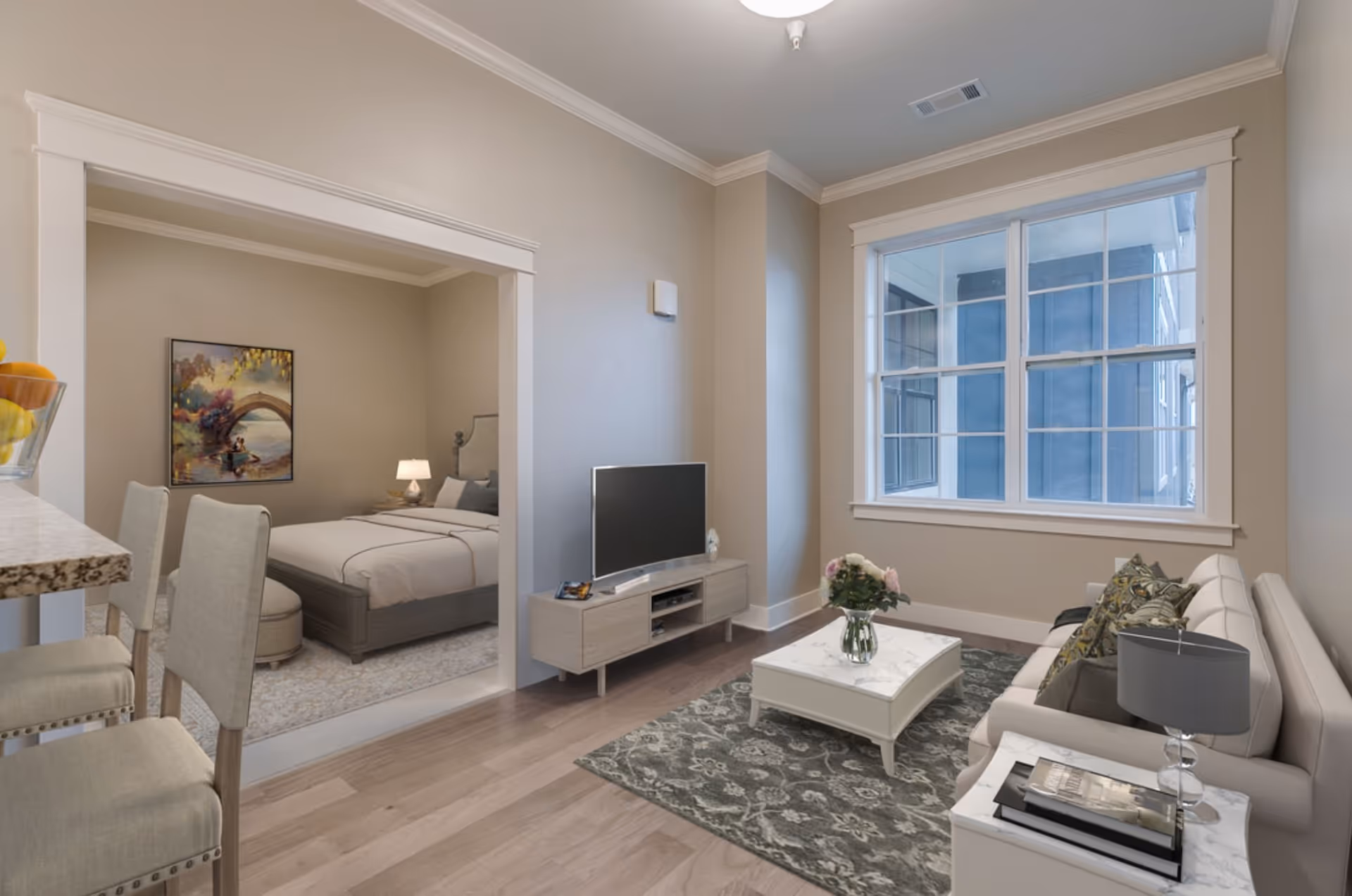 Open-plan living area with a sofa, coffee table, TV and large window adjoining a bedroom.