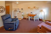 Small senior living apartment interior with two recliners, a round dining table and chairs, and a compact kitchenette.