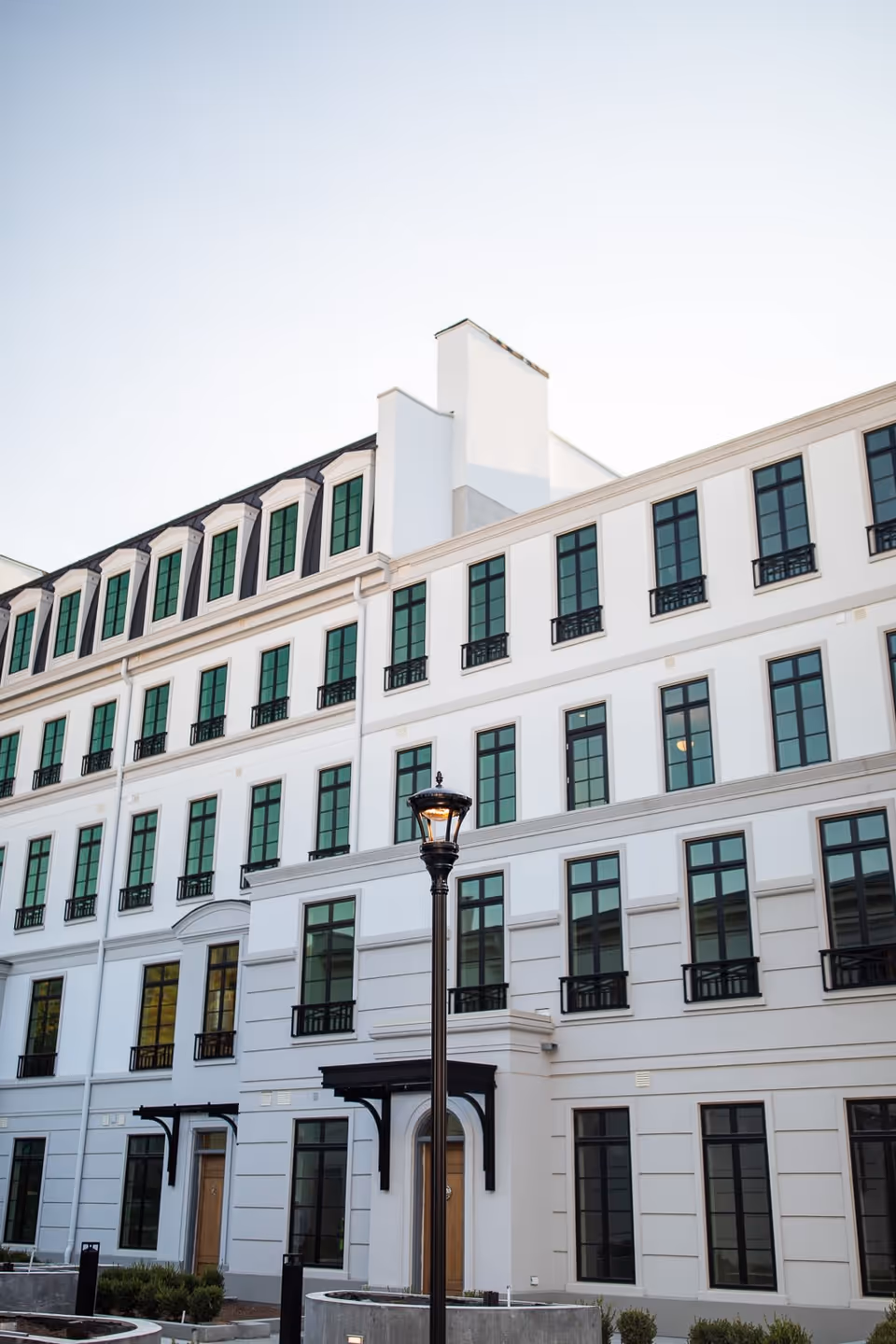 White multi-story residential building facade with rows of green-paned windows and a street lamp in front.