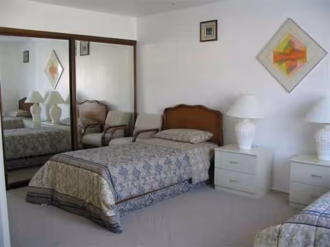 A twin-bedroom setup with two beds, matching nightstands, lamps, and a mirrored closet.