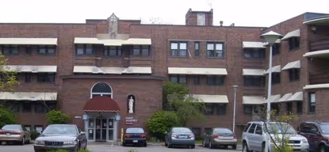 Brick exterior of St Joseph's Manor with arched entrance and parked cars.