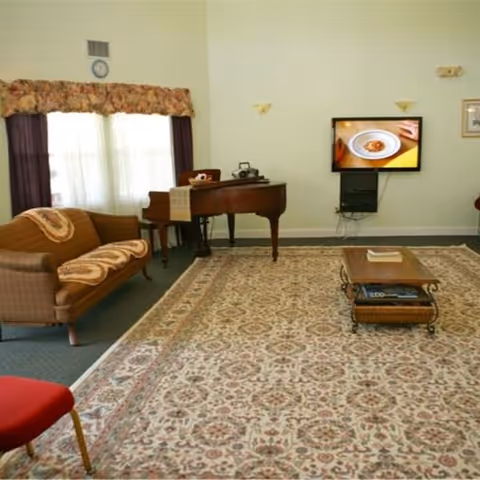 Communal living room featuring a patterned area rug, sofa, grand piano, wall-mounted TV, and coffee table.