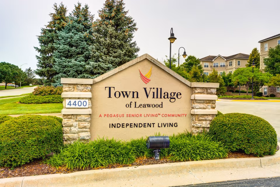 Entrance stone sign that reads "Town Village of Leawood, Independent Living" with an address plaque (4400), landscaping and facility buildings in the background.