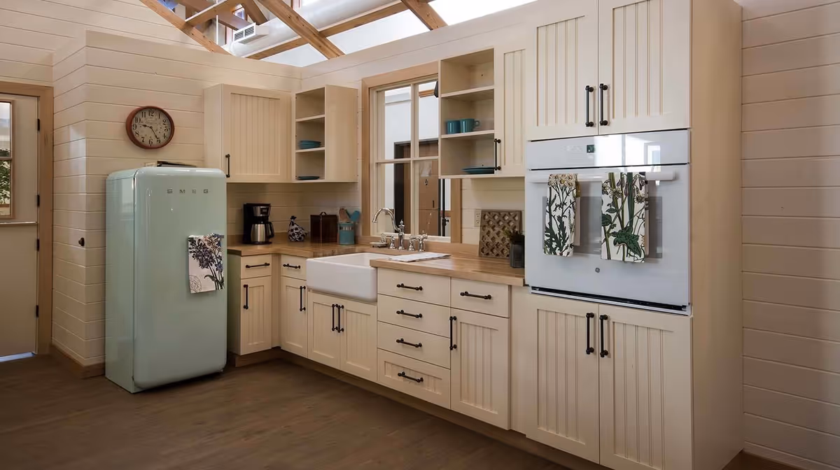 Farmhouse-style kitchen with cream cabinets, a farmhouse sink, a mint-green retro refrigerator, built-in oven, and skylight beams.