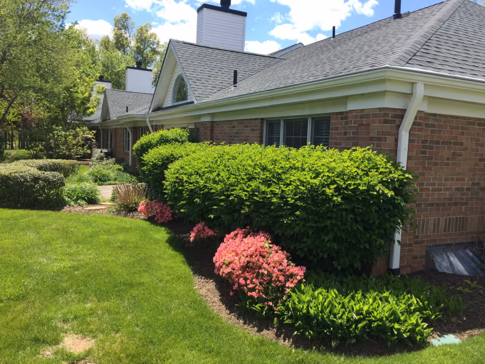 Brick single-story building exterior with a manicured lawn, green shrubs, and pink flowering bushes.