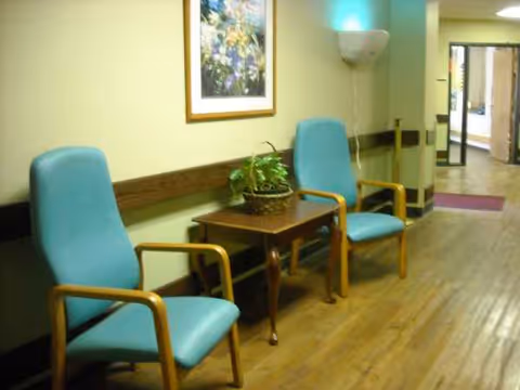 A hallway seating area with teal chairs, a small table, plant, and framed artwork.