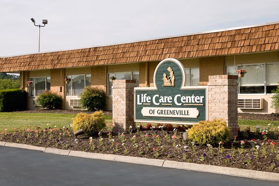 A landscaped front lawn with a sign reading "Life Care Center of Greeneville" in front of a low brick building.