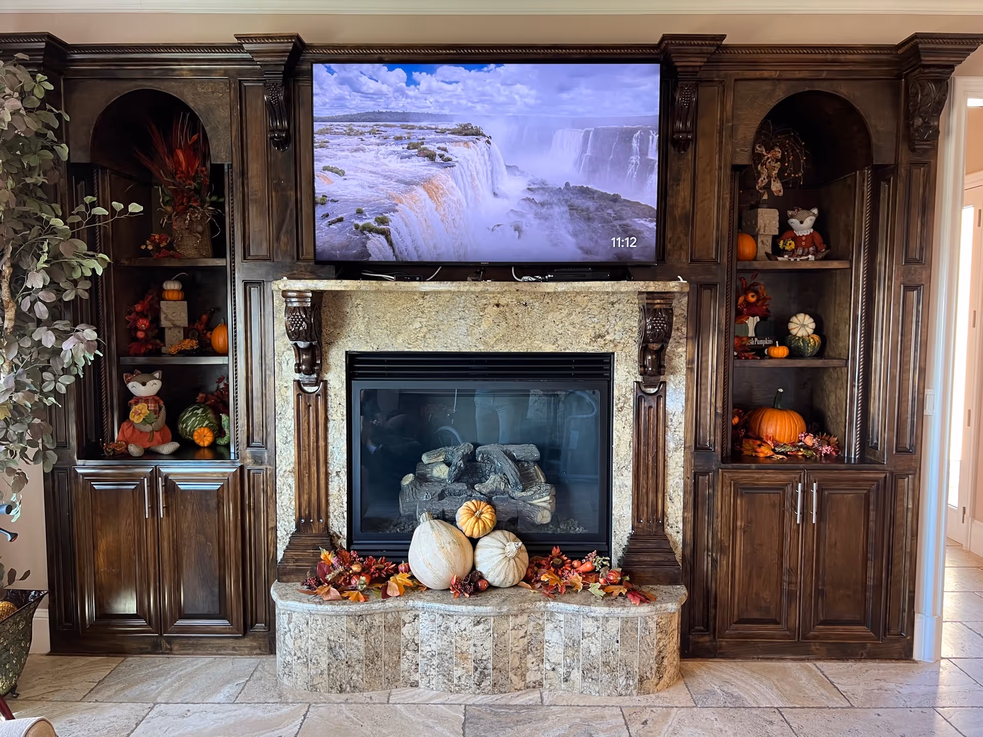 Stone fireplace with a mounted TV and dark wooden built-in shelves decorated with pumpkins and fall décor.