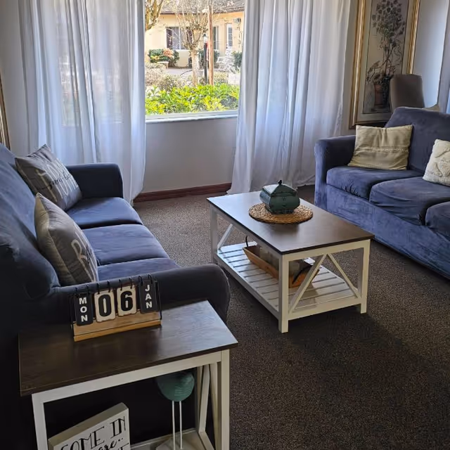 Cozy living room with two blue sofas, a coffee table and end table in front of a window with sheer curtains.