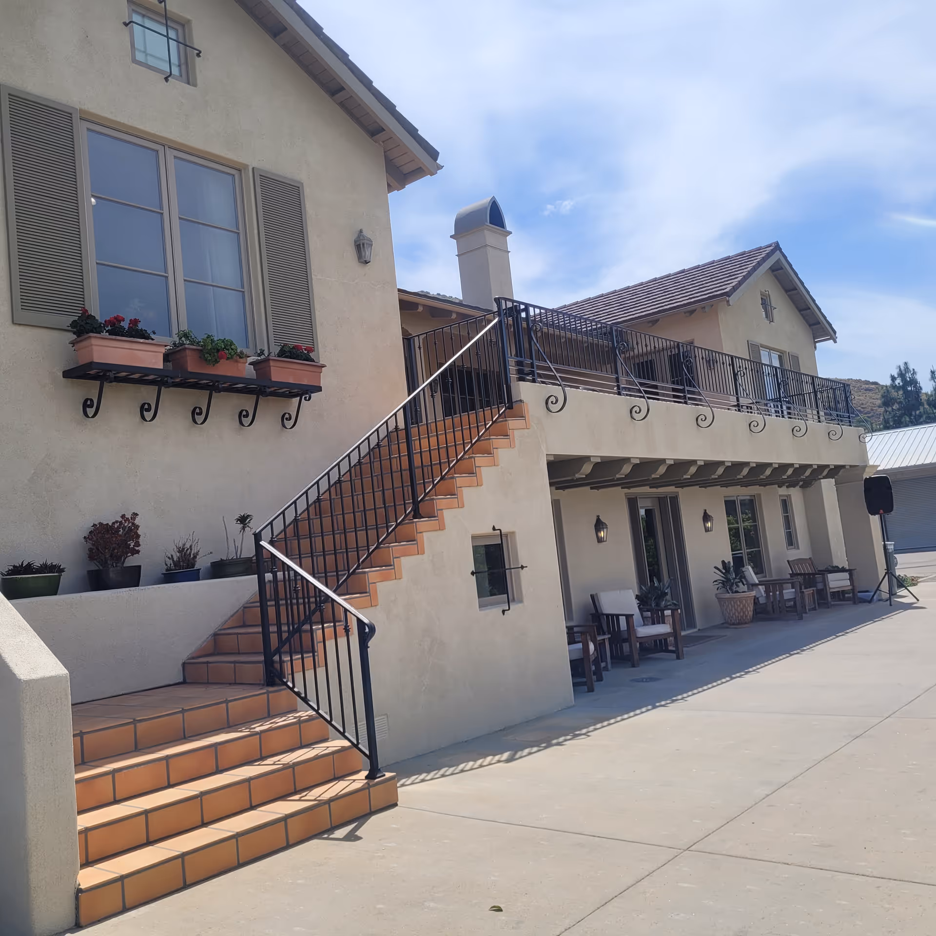 Exterior view of a two-story senior living building with a tiled staircase leading to an upper balcony and outdoor seating below.