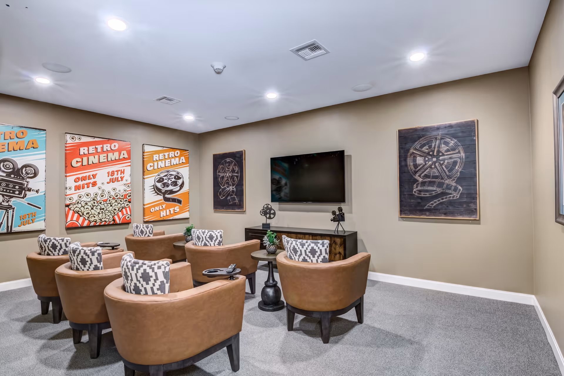 Cozy media lounge with curved leather chairs facing a wall-mounted TV and retro cinema posters on the walls.