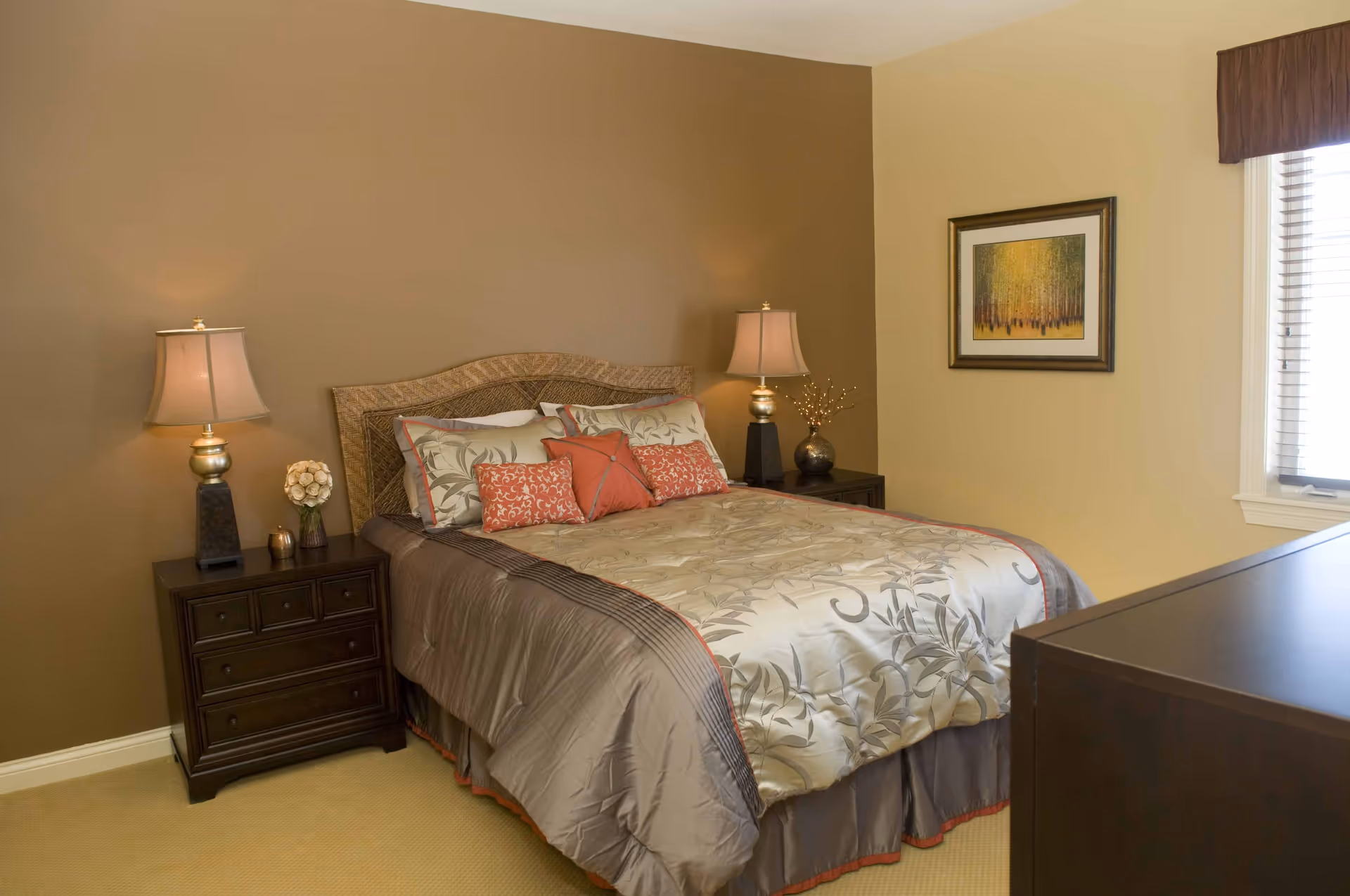 Cozy bedroom with a made bed, matching nightstands and lamps against warm tan walls.