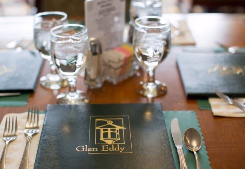 A dining table place setting with menus labeled "Glen Eddy", water goblets, and silverware.