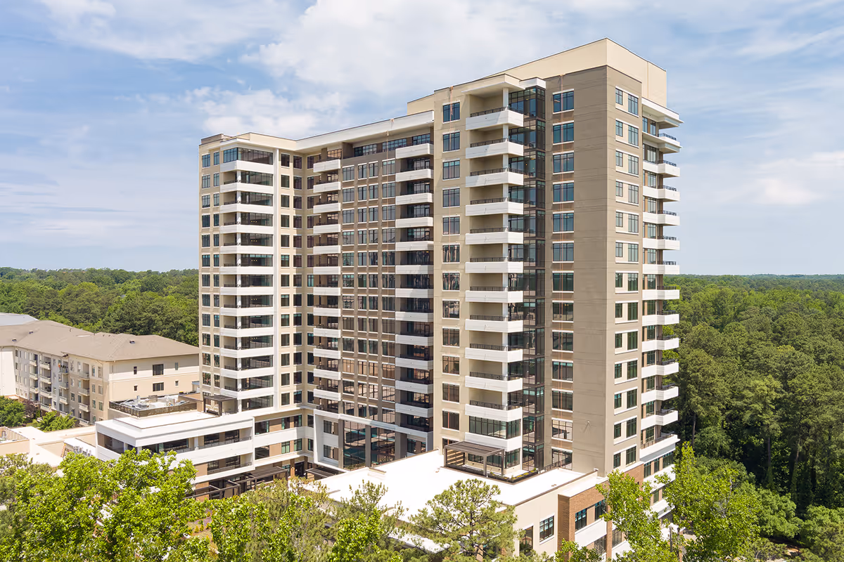 Exterior view of a multi-story senior living facility building surrounded by trees under a partly cloudy sky.