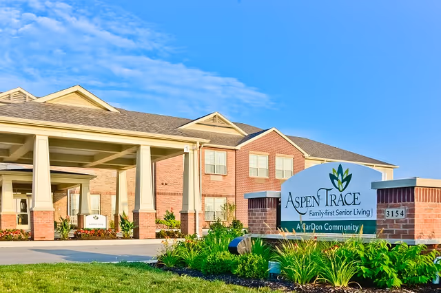 Front entrance and sign for Aspen Trace senior living community with a covered porte-cochère and landscaped grounds.