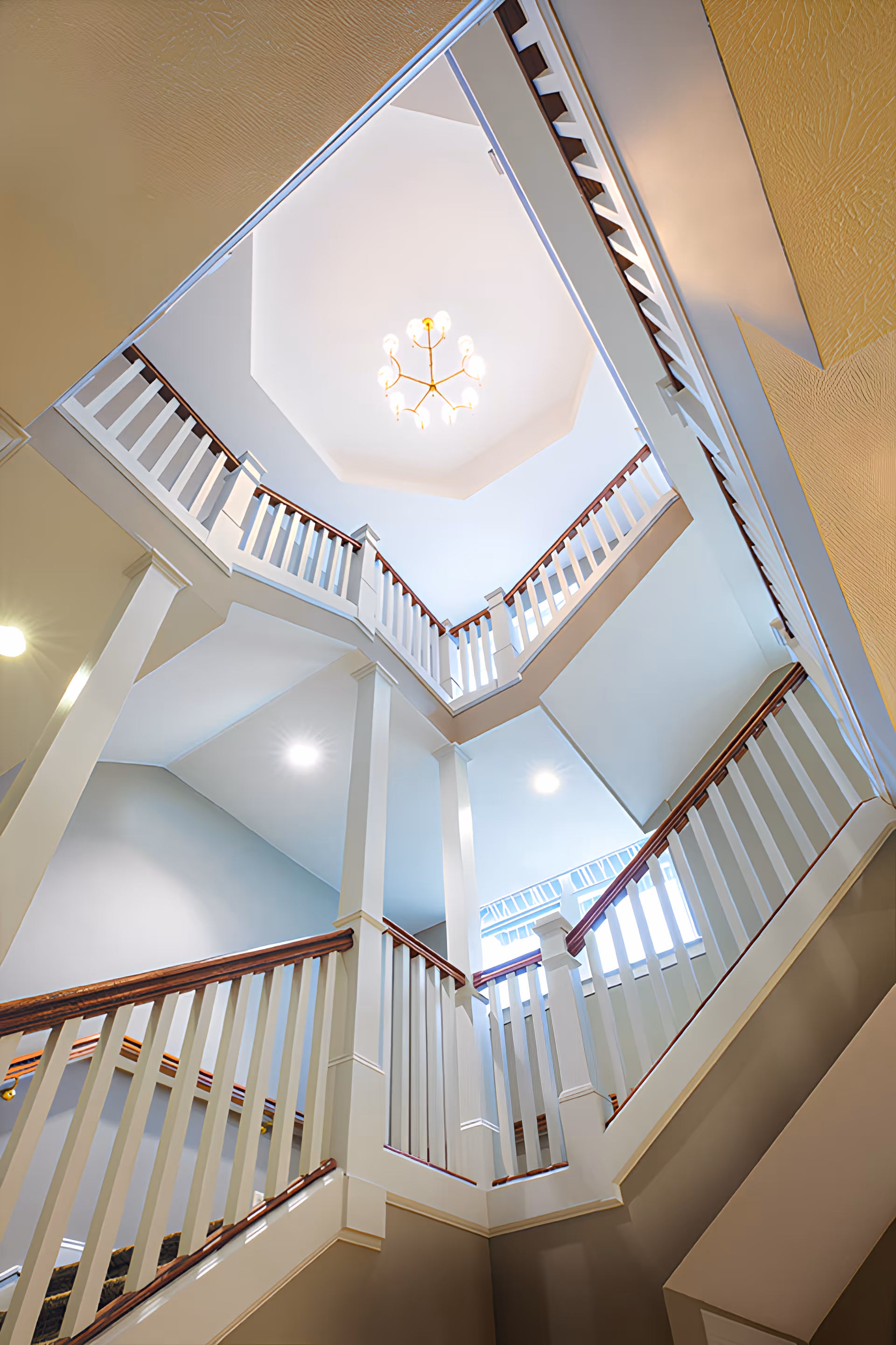 Looking upward through a multi-level interior stairwell with white railings and a chandelier overhead.