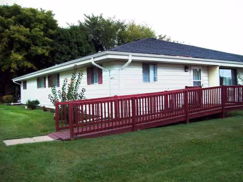 Single-story white senior living facility with a long red ramp to the entrance.