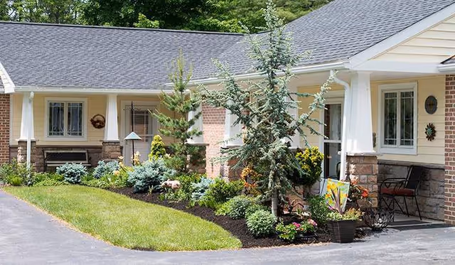 Front exterior of a single-story building with a covered porch, chairs, and landscaped flower beds.