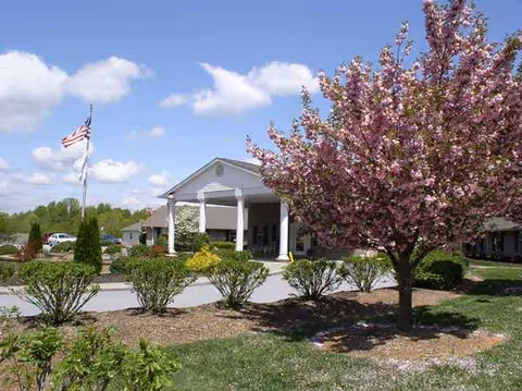 The Laurels of Hendersonville exterior with entrance, blooming tree, flag, and manicured landscaping.