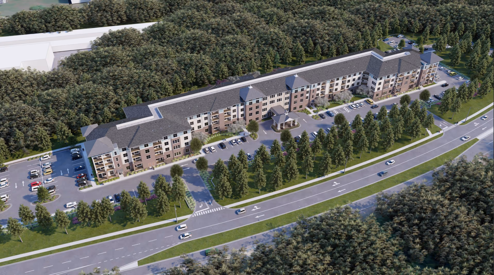 Aerial view of a long multi-story residential building with parking lots, landscaped trees, and a roadway in front.