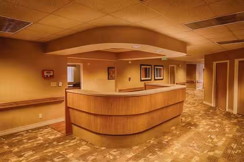 Curved wooden reception desk in a warm, empty hallway of a senior living facility.