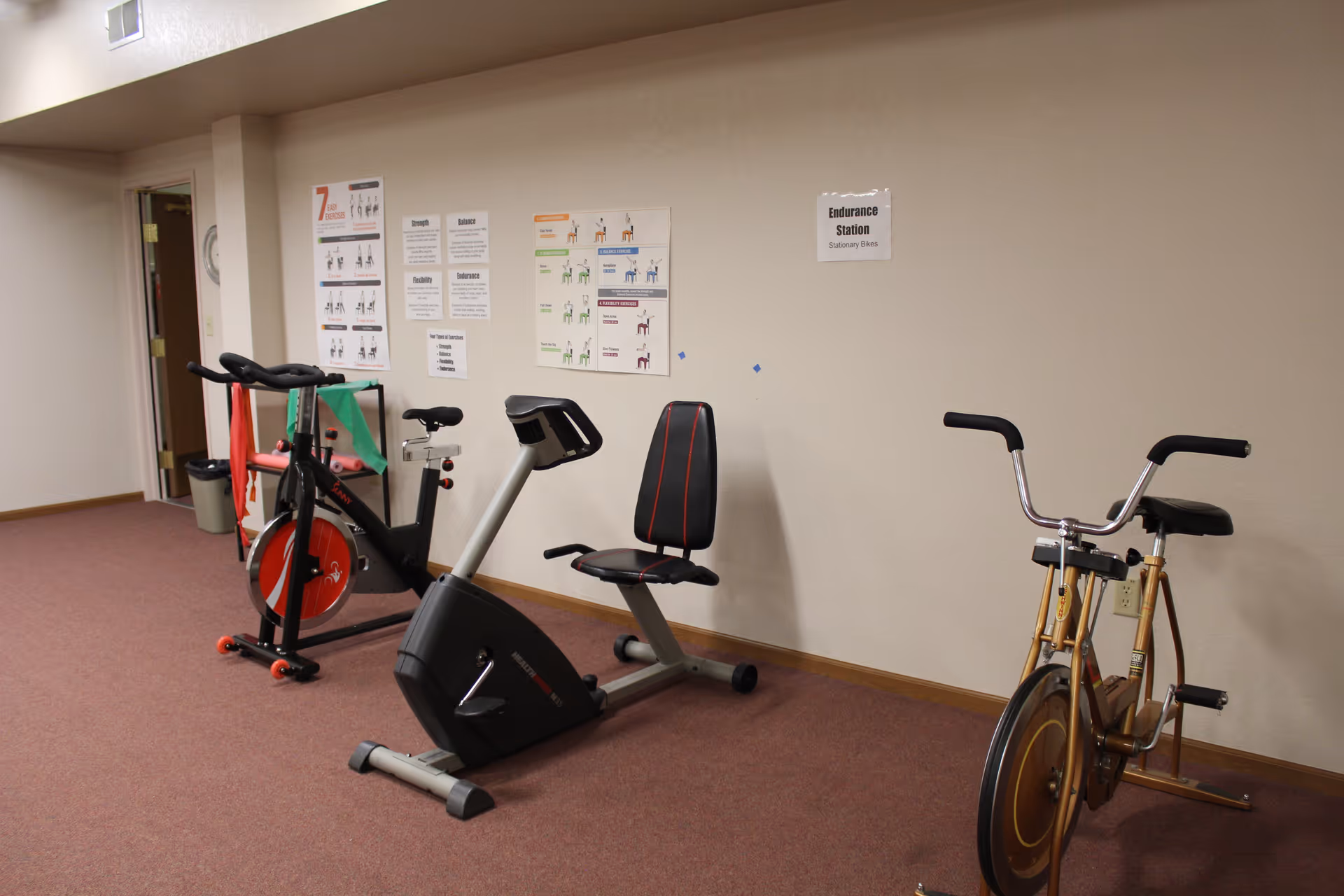 Small exercise room with three stationary bikes against a beige wall and instructional posters.