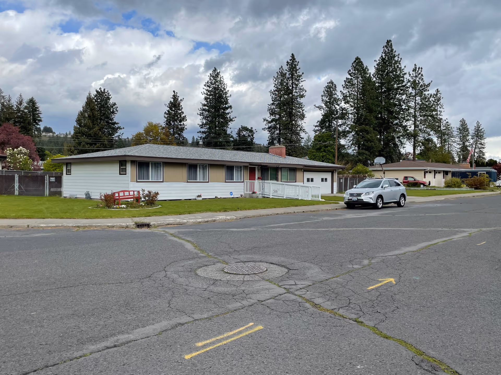 Single-story ranch-style house with a front lawn and a parked car on a residential street under a cloudy sky.