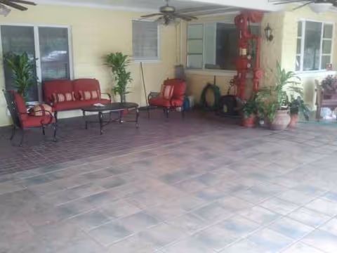 Covered patio with red cushioned seating, potted plants, and tiled floor.