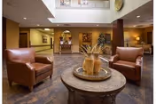 Lobby seating area with two brown leather chairs around a round table topped with decorative vases beneath an atrium.