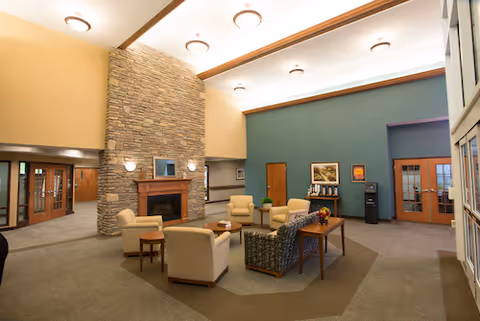 Spacious communal lounge with armchairs and sofas arranged around a stone fireplace beneath high, beamed ceilings.