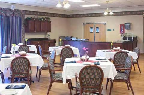 Senior living dining room with round tables, chairs, and a service counter in the background.