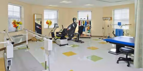 Bright rehabilitation gym with exercise machines and therapy equipment in a senior living facility.