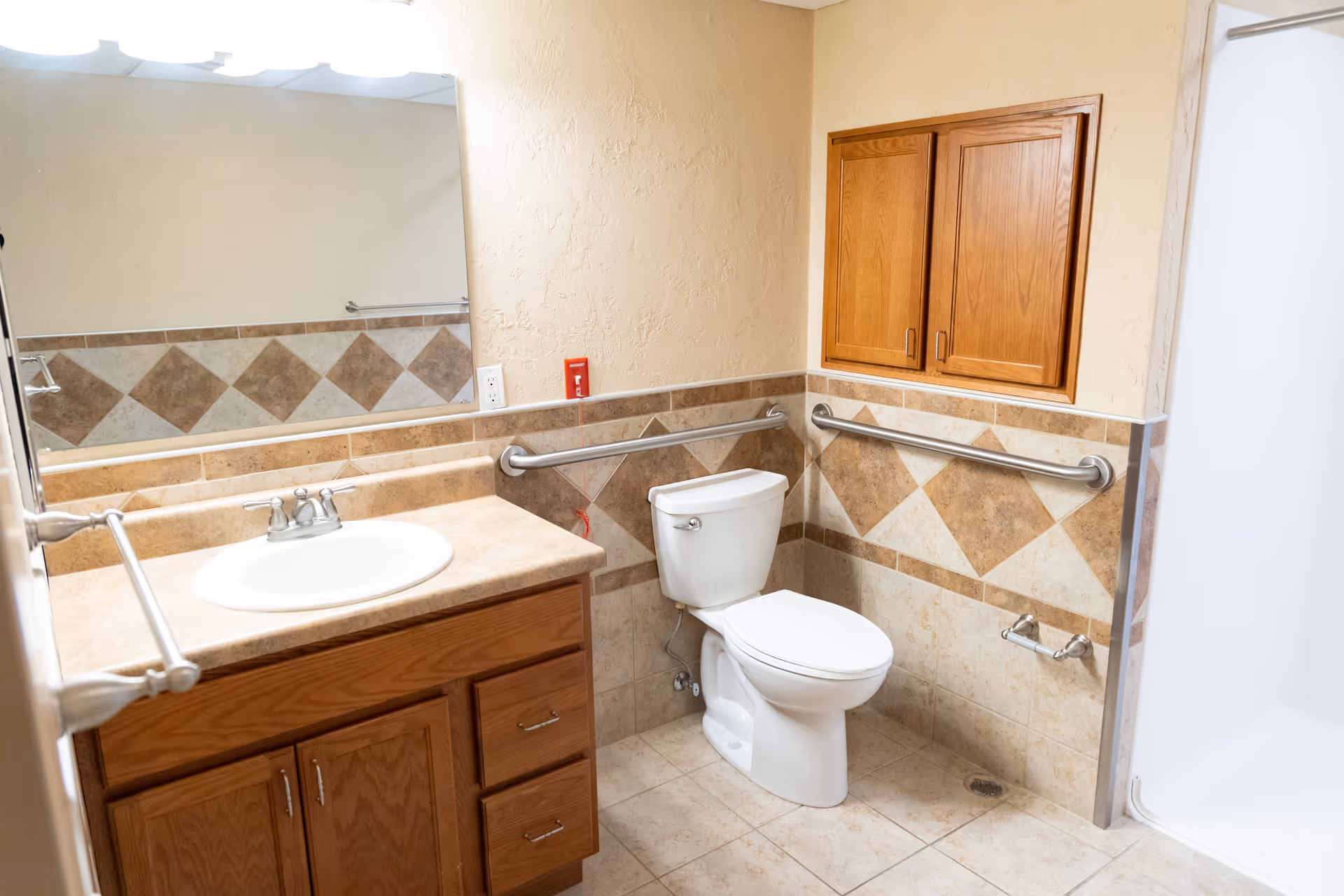 Accessible bathroom with a sink and vanity, toilet, grab bars, tiled walls and a shower stall.