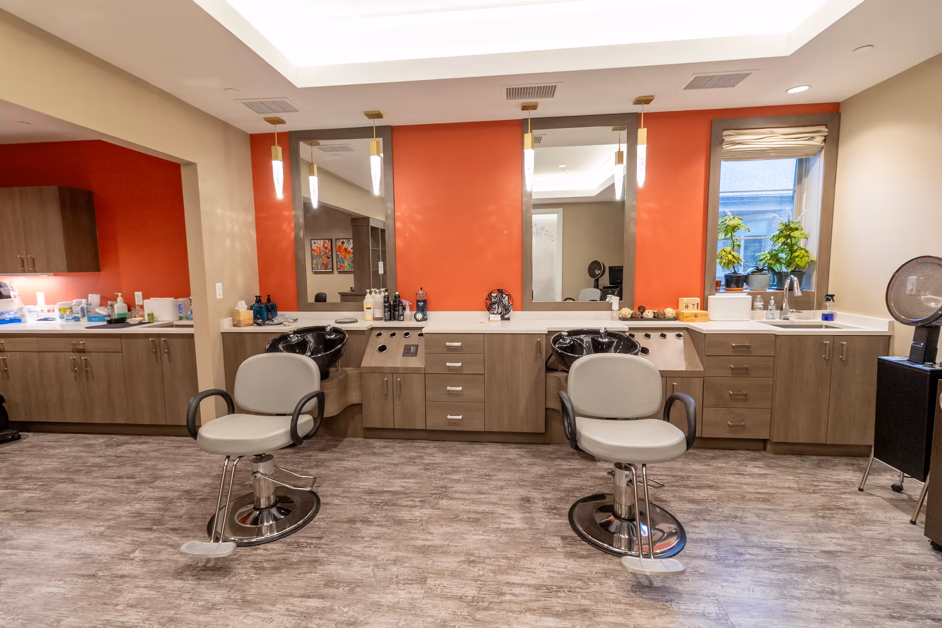 Interior salon with two styling chairs, shampoo bowls, mirrors, and cabinetry against an orange accent wall.