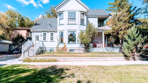Front view of a two-story white house with bay windows, a covered porch, and a lawn with sidewalk in front.