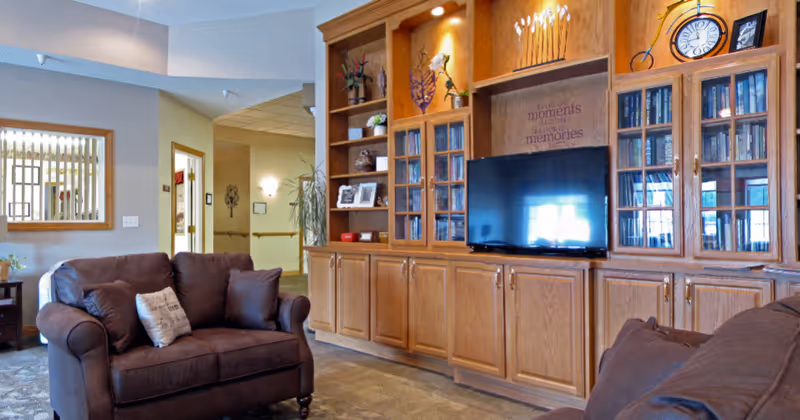 Comfortable lounge with brown upholstered chairs facing a large wooden built-in entertainment center and TV.
