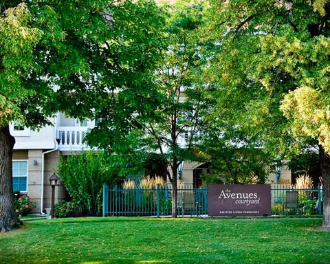 Exterior view of The Avenues Courtyard with lush trees, lawn, and a front fence sign.