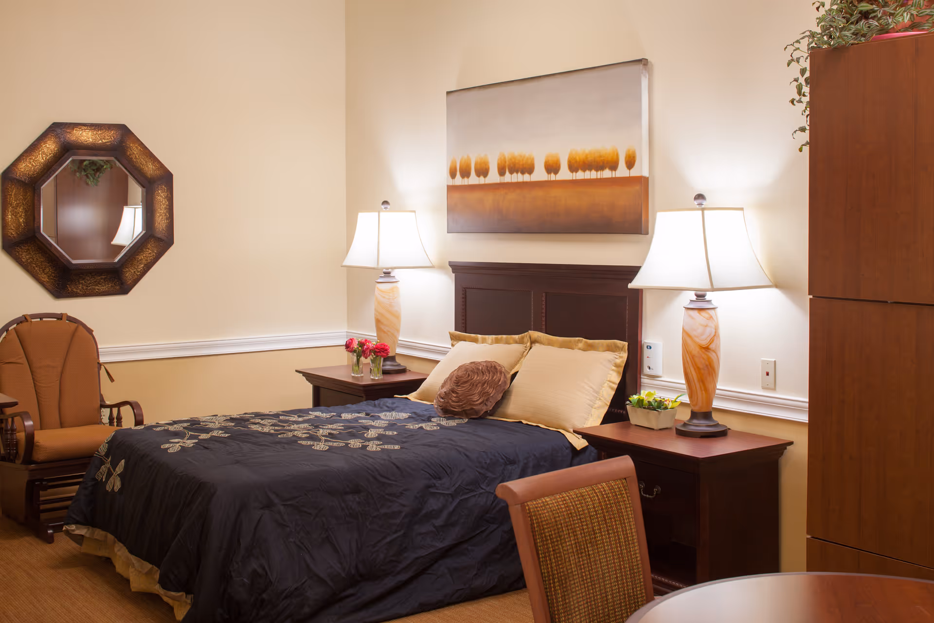 Cozy bedroom featuring a bed with a dark comforter, two bedside tables with lamps, wall art, and seating.